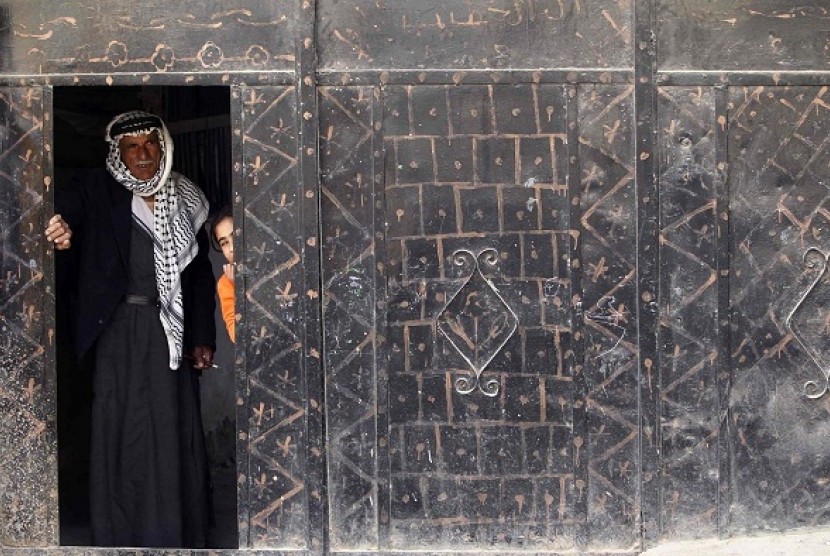 A Palestinian man and girl stand at a doorway and watch as stone-throwing Palestinian protesters clash with Israeli security officers in the West Bank village of Tamoun, near the West Bank city of Jenin January 1, 2013.   