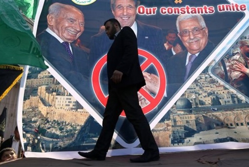 A Palestinian man walks past a poster showing Israeli President Shimon Peres, from left, US Secretary of State John Kerry and Palestinian President Mahmoud Abbas in the northern Gaza Strip, Friday, Feb. 7, 2014.