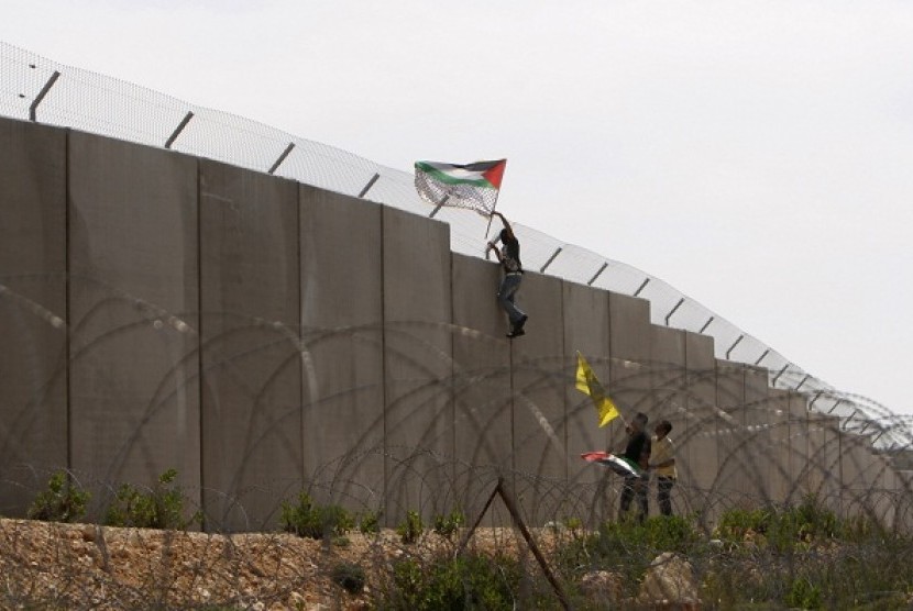 A protester hangs a Palestinian flag on the controversial Israeli barrier during a protest over its construction in the West Bank village of Bilin near Ramallah, recently.