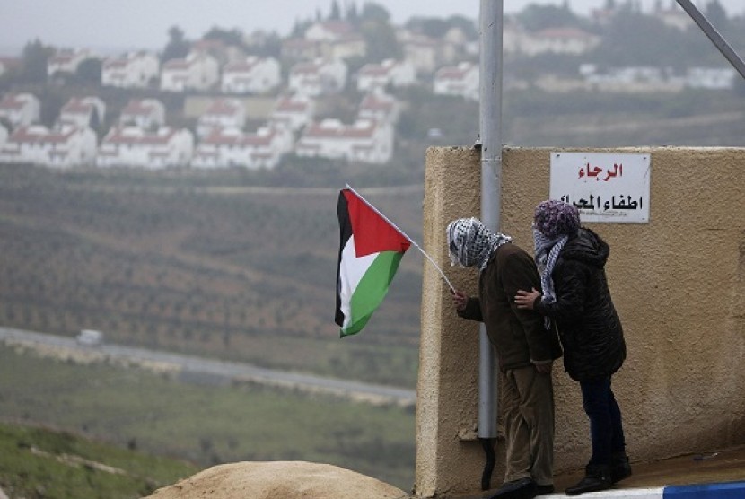 A protester holds the Palestinian flag with the Jewish settlement of Halamish seen in the background during clashes between stone-throwing protesters and Israeli soldiers in the West Bank village of Nabi Saleh, near Ramallah December 21, 2012. (illlustrati