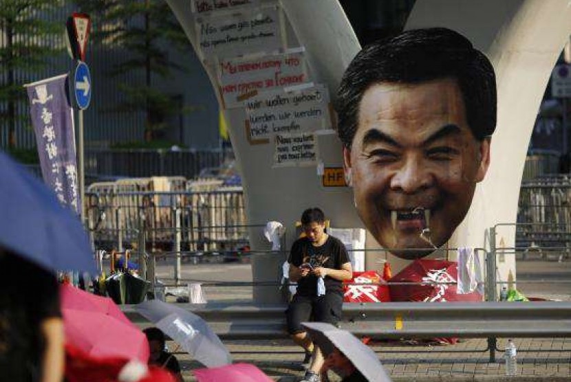 A protester sits next to a defaced cut-out of Hong Kong Chief Executive Leung Chun-ying while blocking a street outside the government headquarters in Hong Kong September 30, 2014. 