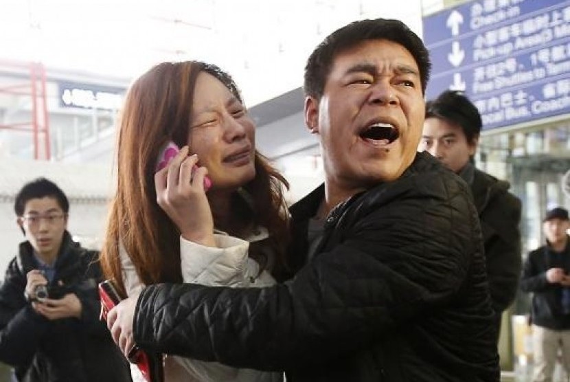 A relative (woman in white) of a passenger onboard Malaysia Airlines flight MH370 cries as she talks on her mobile phone at the Beijing Capital International Airport, March 8, 2014.