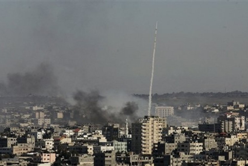 A rocket fired by Palestinian activists at southern Israel leaves a thin trail of white smoke, as smoke caused by explosions from Israeli forces' operations rises from buildings on the outskirts of Gaza City.  (File photo 2009)