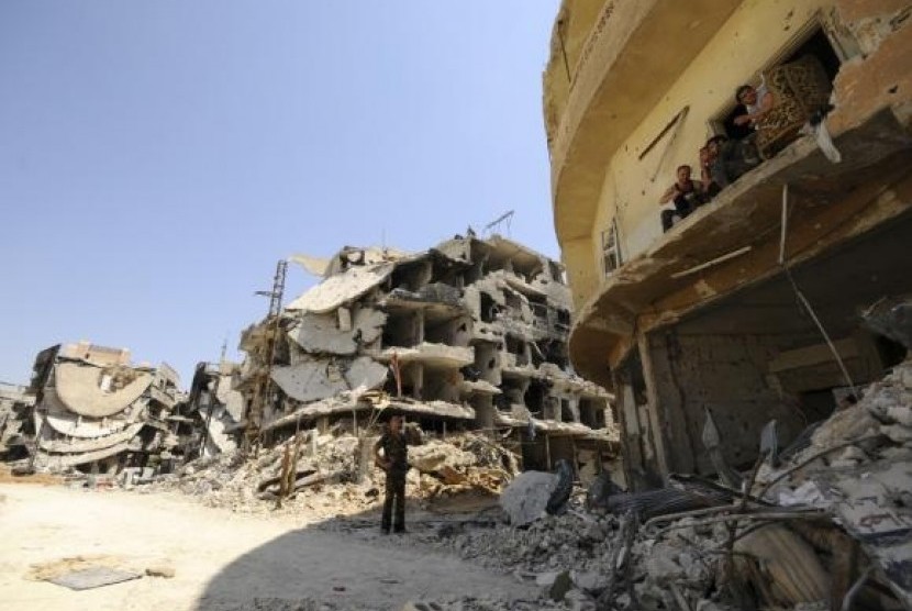 A Syrian army soldier loyal to Syria's President Bashar al-Assad chats with fellows sitting on a balcony of a damaged building in Mleiha, on August 15, 2014.