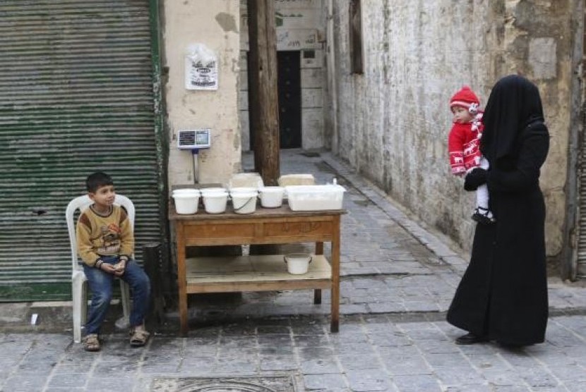 A woman carries a child as she walks past a boy selling yogurt along a street in Aleppo's Bab al-Hadeed district December 10, 2014.