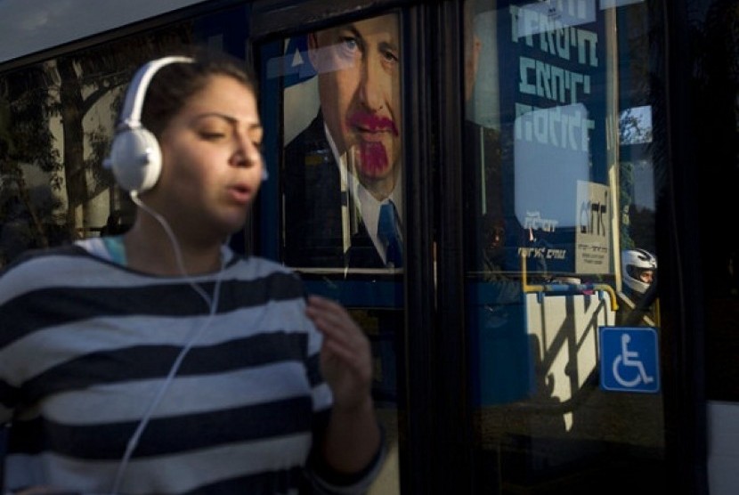 A woman jogs past a vandalized election campaign billboard of Israeli Prime Minister and Likud Party leader Benjamin Netanyahu that is reflected on a bus window in Tel Aviv, Israel.