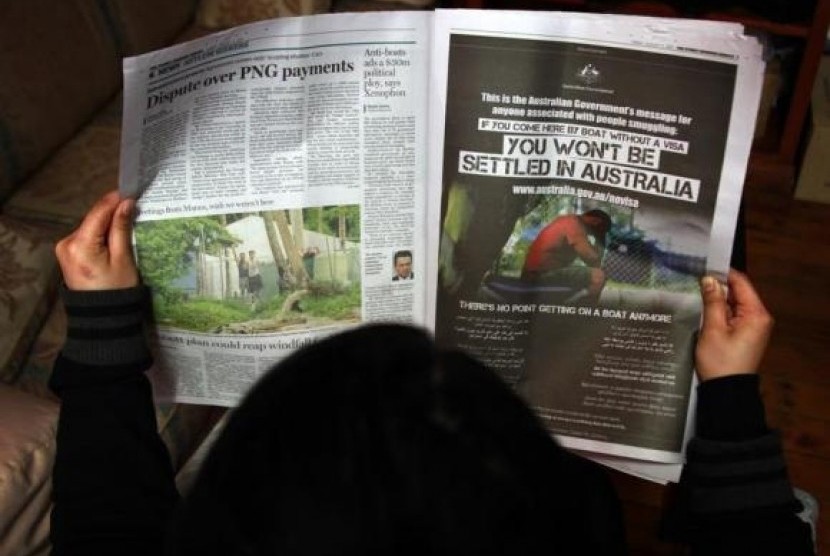 A woman reads a newspaper containing an advertisement (R) publicising the Australian government's new policy on asylum seekers arriving by boat, in Sydney August 2, 2013.