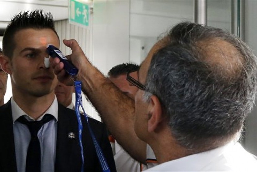 Airport physician Dr. Bargain (right) demonstrates the use of a thermometer to highlight measures to screen passengers for the Ebola virus, at the Charles de Gaulle airport, north of Paris, France, Friday, Oct. 17, 2014. 