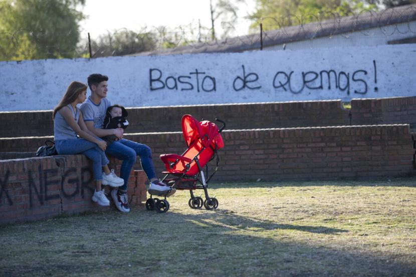 Alejandro Rica, kanan, menggendong putranya yang berusia tiga bulan, Teo, saat dia duduk bersama temannya Lara Barretos, di sebelah grafiti yang bertuliskan dalam bahasa Spanyol. Bank sentral Argentina menaikkan suku bunga acuan negara itu 550 basis poin menjadi 75 persen pada Kamis (15/9/2022). 