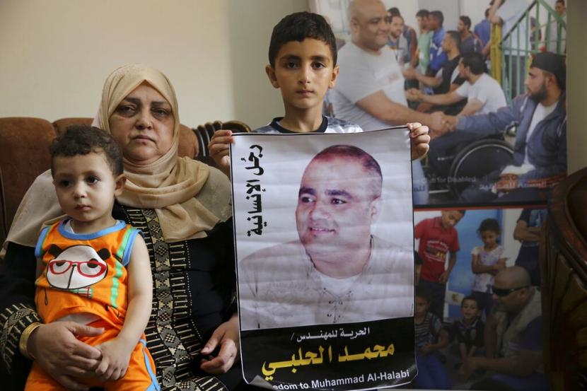 Amal el-Halabi menggendong cucunya Fares sementara cucunya Amro, 7, memegang foto ayahnya Mohammed el-Halabi, direktur Gaza dari badan amal internasional World Vision, yang dihukum oleh pengadilan Israel karena mengalihkan jumlah uang ke Hamas, di rumahnya rumah keluarga di Kota Gaza, 8 Agustus 2016. Pengadilan Israel menjatuhkan hukuman 12 tahun penjara kepada el-Halabi setelah dia dinyatakan bersalah awal tahun ini atas beberapa tuduhan terorisme dalam kasus tingkat tinggi di mana penyelidikan independen tidak menemukan bukti kesalahan.