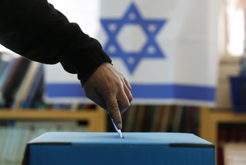 An Israeli flag is seen in the background as a man casts his ballot for the parliamentary election at a polling in the West Bank Jewish settlement of Ofra, north of Ramallah January 22, 2013. 