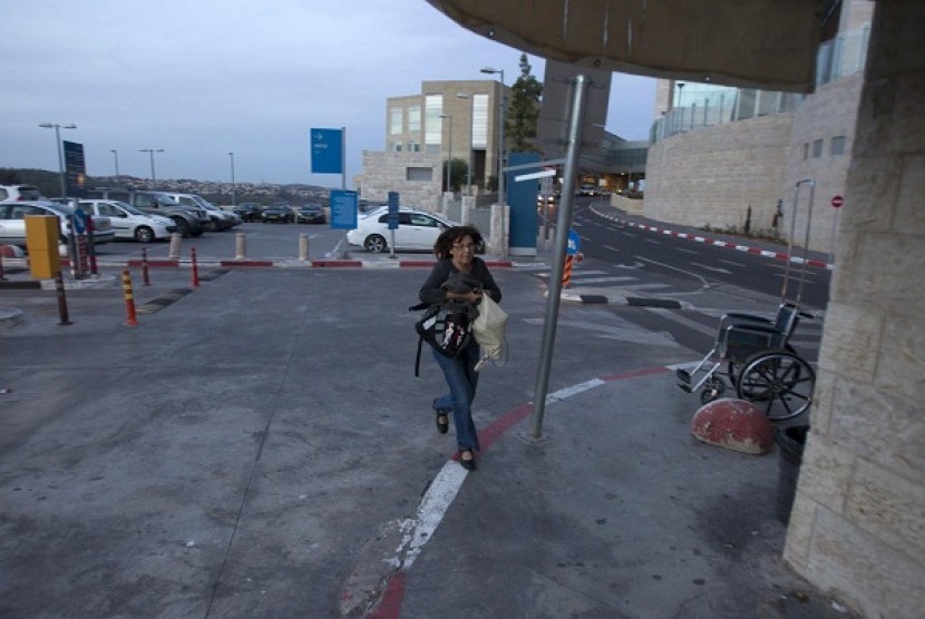 An Israeli woman runs to take cover as an air raid siren warns of incoming rockets at the parking lot of a hospital in Jerusalem November 16, 2012. 