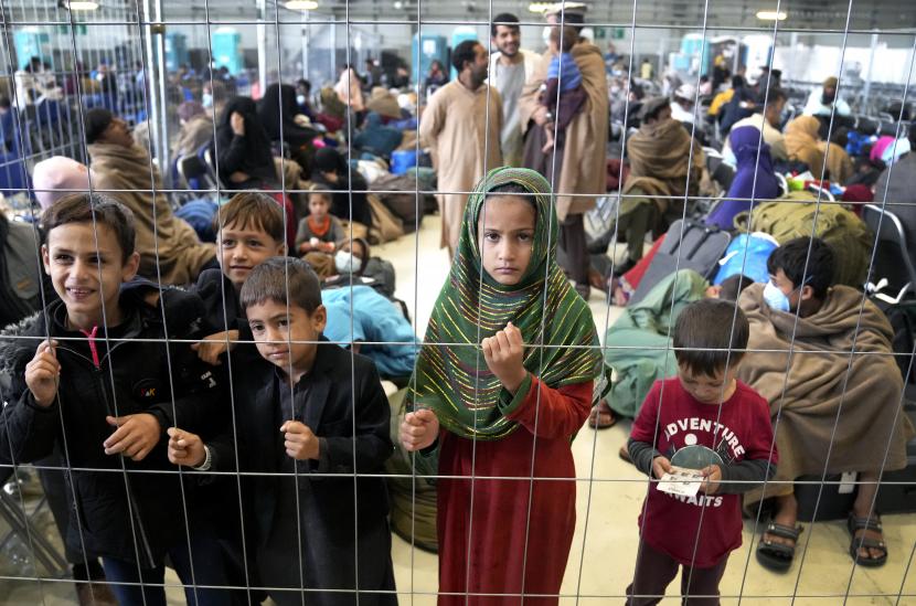  Anak-anak berdiri di belakang pagar di hanggar saat mereka menunggu keberangkatan mereka di Pangkalan Udara AS Ramstein di Ramstein, Jerman, Senin, 30 Agustus 2021. Komunitas militer Amerika terbesar di luar negeri menampung ribuan pengungsi Afghanistan di sebuah kota tenda di pangkalan udara . 