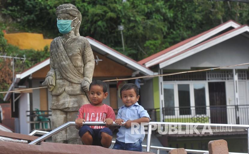 Anak-anak bermain di dekat patung Syamsul Bahri yang dipasangkan masker di Batang Arau, Padang, Sumatra Barat, Sabtu (30/5/2020). Orang tua harus melindungi anaknya dari paparan Covid-19.