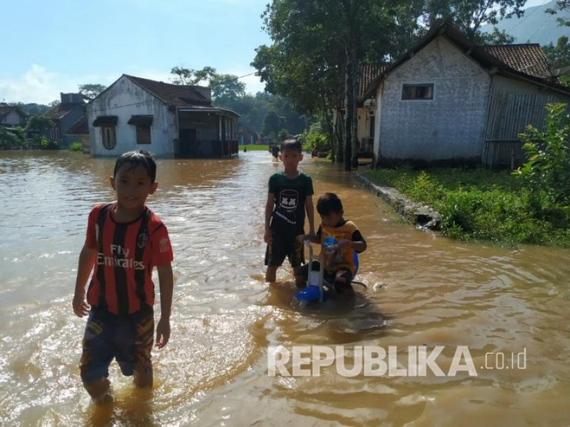 Anak-anak bermain di jalan yang tergenang banjir