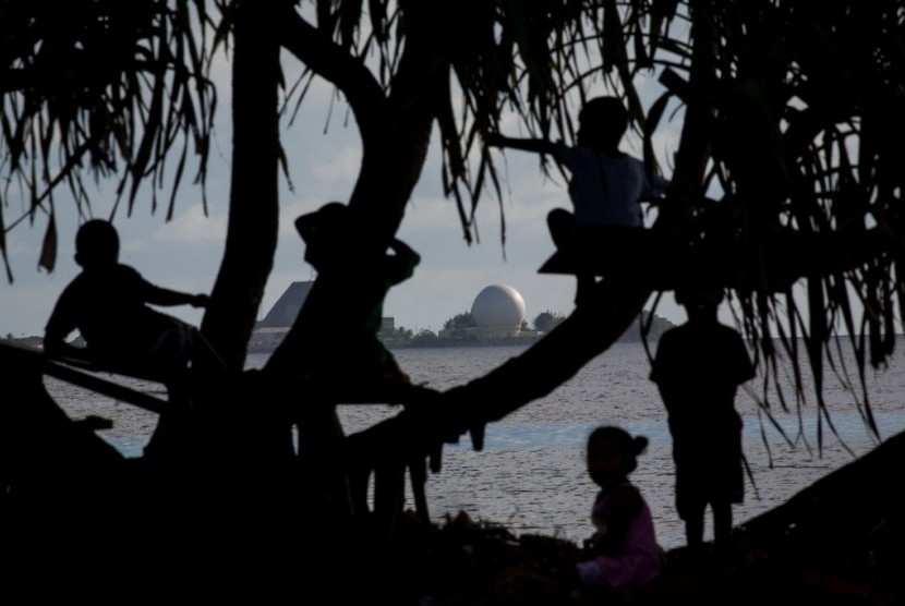 Anak-anak bermain di sebuah pohon di Ebeye berlatar belakang Ronald Reagan Ballistic Missile Defense Test Site (tempat pengujian rudal) di Kwajalein.