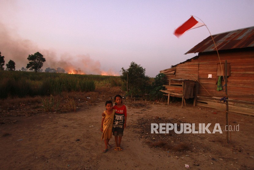 Anak-anak berpose di halaman rumah dengan latar belakang kebakaran lahan gambut di Kecamatan Bati-Bati, Kabupaten Tanah Laut, Kalimantan Selatan, Ahad (1/9/2019). 
