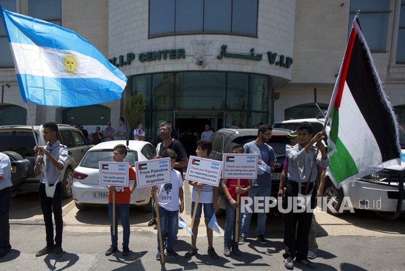 Anak-anak lelaki Palestina memegang spanduk di depan kantor perwakilan Argentina di kota Ramallah, Tepi Barat, Rabu (6/6). Argentina telah membatalkan pertandingan persahabatan melawan Israel menyusul protes oleh kelompok pro-Palestina.