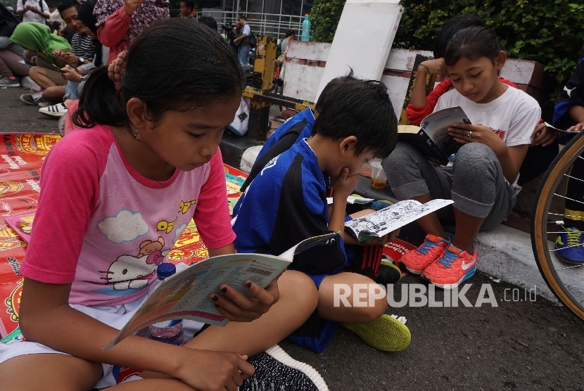  Anak-anak membaca buku di stand komunitas Buku 100 Desa saat berlansungya Car Free Day di Bundaran HI, Jakarta, Ahad (2/4). 