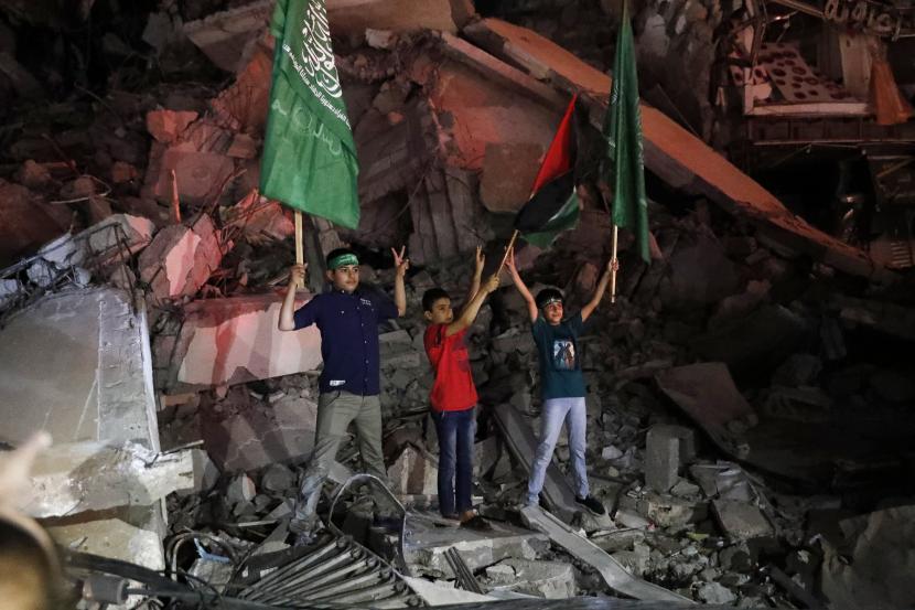 Anak-anak Palestina mengibarkan Hamas hijau dan bendera nasional mereka saat mereka berdiri di atas puing-puing bangunan yang hancur saat merayakan perjanjian gencatan senjata antara Israel dan Hamas di Kota Gaza, Jumat dini hari, 21 Mei 2021.
