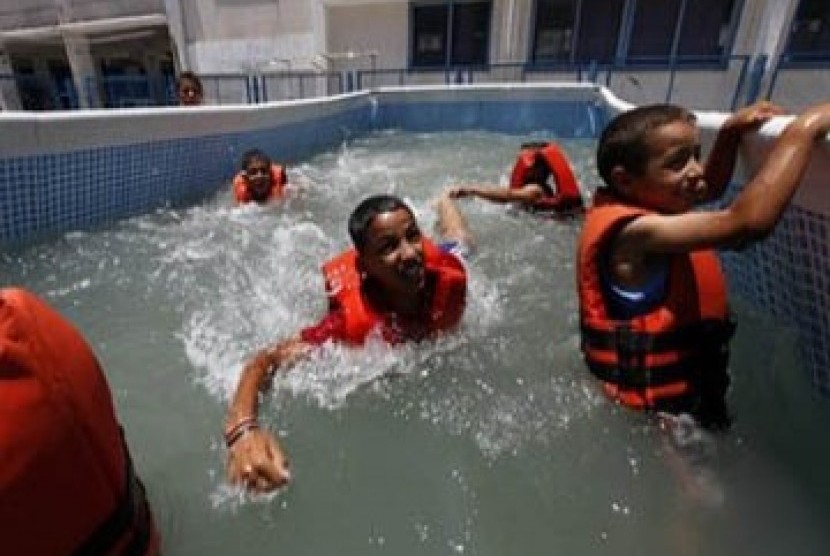 Anak-anak tengah menikmati berenang di kolam plastik di kemah musim panas milik PBB.