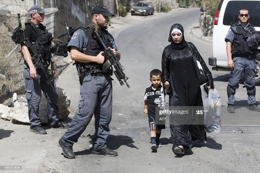 Anak Palestina bersama ibunya melewati penjagaan tentara Israel yang bersenjata lengkap.