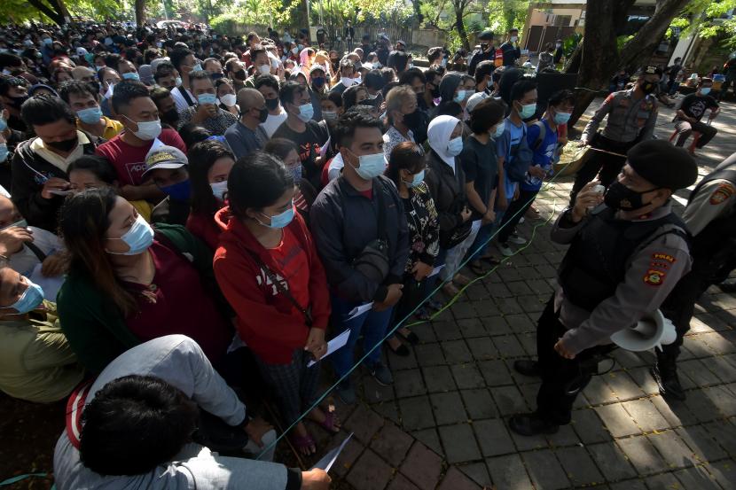 Anggota Polisi mengarahkan ribuan warga yang antre vaksinasi COVID-19 massal di Denpasar, Bali.