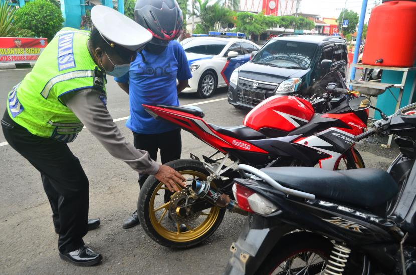 Anggota polisi menilang pengendara motor pengguna knalpot racing saat penertiban oleh jajaran Satlantas Polres Kudus, Jawa Tengah, Senin (17/1/2022).