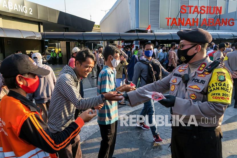 Polisi membagikan masker pada calon penumpang di Stasiun Tanah Abang, Jakarta Pusat.
