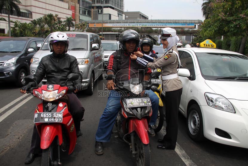   Anggota polwan Bripka Novi memperbaiki tali helm pengendara motor di lampu merah Bundaran HI, Jakarta Pusat, Senin (25/11).  (Republika/Yasin Habibi)