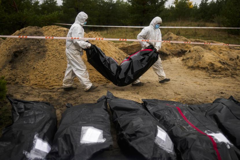 Anggota tim forensik membawa kantong plastik dengan tubuh di dalamnya saat mereka bekerja di penggalian di kuburan massal di Lyman, Ukraina, Selasa, 11 Oktober 2022.