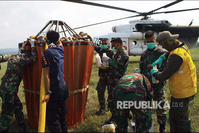 Anggota TNI bersama tim Kementerian Kesehatan mengisi cairan desinfektan di wadah khusus untuk dibawa helikopter BNBP disemprotkan melalui udara dengan metode water bombing  pada dua lokasi gempa likuifaksi, Balaroa dan Petobo di Bandara Mutiara Sis Al Jufri Kota Palu, Sulawesi Tengah, Kamis (18/10). 