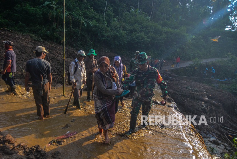 Anggota TNI membantu warga saat menyebrangi jalan yang berlumpur akibat longsor di Desa Santanamekar, Kabupaten Tasikmalaya, Jawa Barat, Senin (2/3/2020).(Antara/Adeng Bustomi)