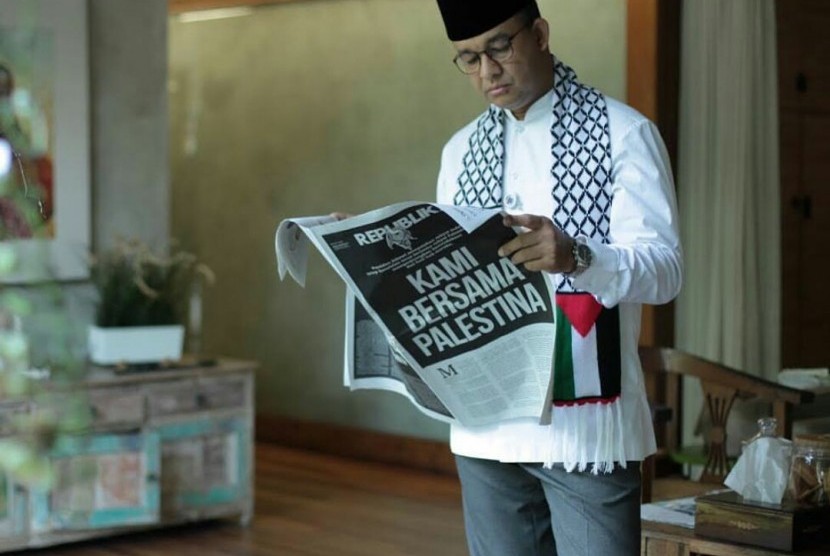 Anies Baswedan mengenakan syal berbendara Palestina sambil membaca koran Republika, Jumat (8/12).