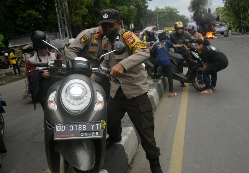 Aparat kepolisian membantu pengendara mengangkat motornya melewati pembatas jalan saat berlangsung aksi unjuk rasa mahasiswa di Makassar, Sulawesi Selatan, Jumat (28/10/2022). Pelajar yang kedapatan mengendarai motor tanpa memiliki SIM akan diamankan kendaraannya.