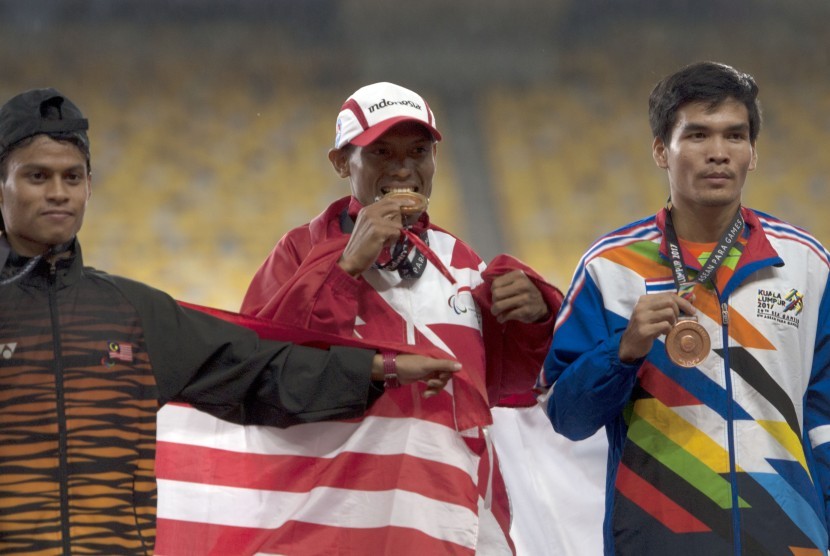 Atlet Indonesia Endi Nurdin Tine (tengah) menggigit medali emas yang diraihnya setelah menjuarai nomor lari 800 meter putra Asean Para Games XI Kuala Lumpur, di Stadion Bukit Jalil, Kuala Lumpur, Malaysia, Selasa (19/9). 