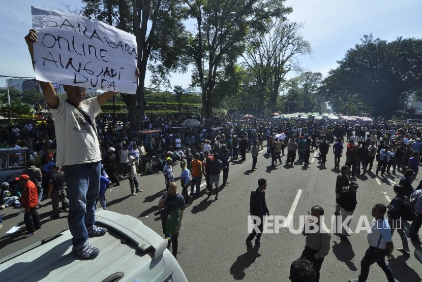 Awak angkot memperlihatkan poster pada aksi angkutan kota (angkot) dan taksi Kota Bandung melakukan aksi unjuk rasa dan mogok massal di depan Gedung Sate, Jalan Diponegoro, Kota Bandung, Kamis (9/3).