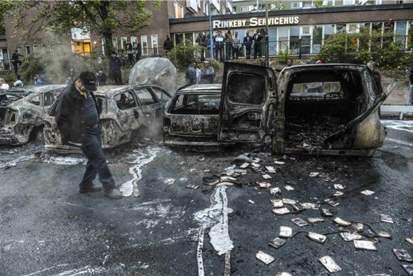 Bangkai mobil teronggok setelah massa membakarnya dalam kerusuhan yang terjadi di daerah pinggiran Rinkeby, Stockholm, Swedia, Kamis (23/5). 