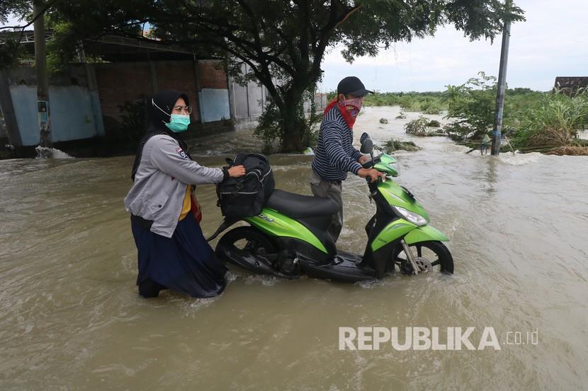 Ilustrasi. Warga mendorong motor melintasi banjir di Jalan Benjeng, Kabupaten Gresik, Jawa Timur, Senin (14/12/2020).