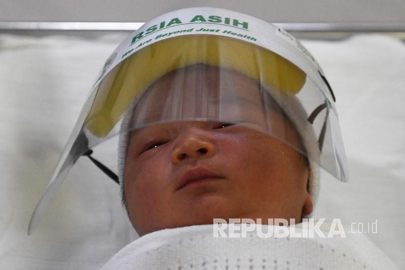 Bayi mengenakan pelindung muka atau face shield. 