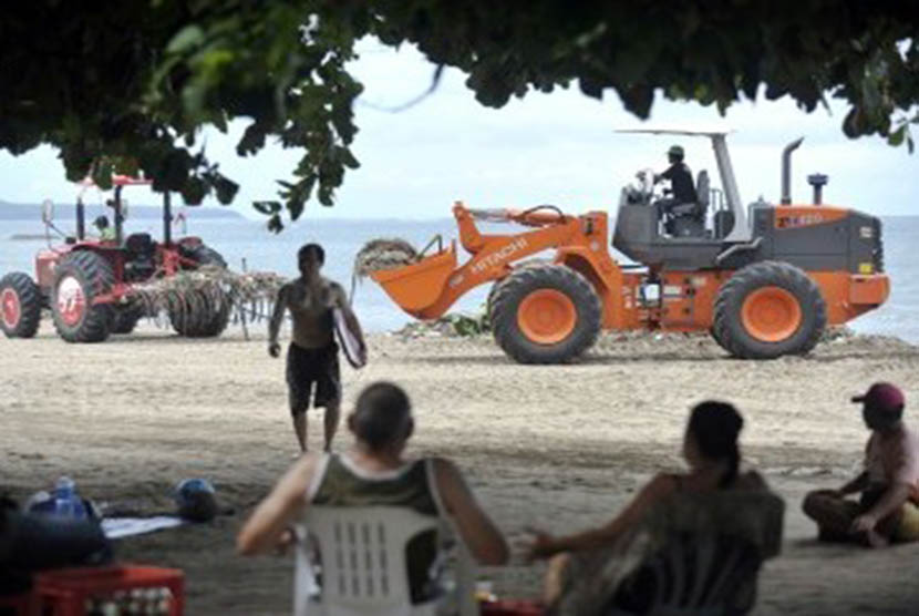 Beberapa wisatawan berada di dekat dua alat berat yang digunakan untuk mengangkut sampah yang memenuhi sekitar Pantai Kuta, Bali, Jumat (30/12). (ANTARA/Nyoman Budhiana)