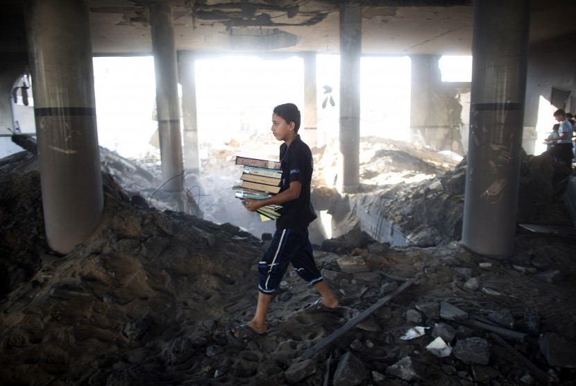 Bocah Palestina membawa buku agama yang ia selamatkan dari sebuah masjid di Gaza setelah serangan Israel, Sabtu (9/8)