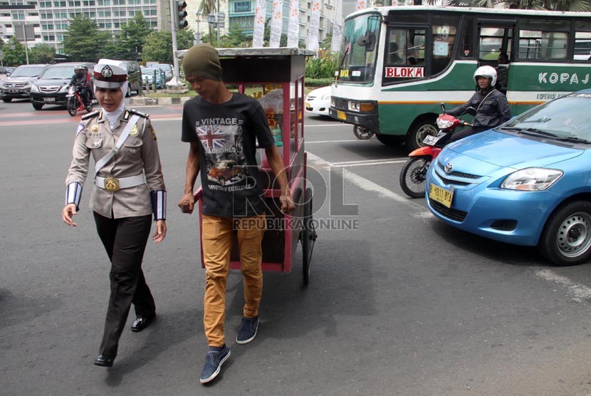  Bripka Novi dengan mengenakan seragam polisi berjilbab membantu pedagang menyeberang jalan di lampu merah Bundaran HI, Jakarta Pusat, Senin (25/11).  (Republika/Yasin Habibi)