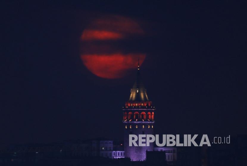 Bulan purnama terlihat di belakang Menara Galata di waktu menjelang fajar di Istanbul, Turki pada 6 Mei 2020.