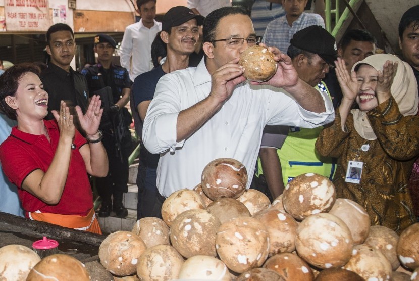 Calon Gubernur DKI Jakarta Anies Baswedan (tengah) meminum air kelapa saat kampanye di tengah pasar 