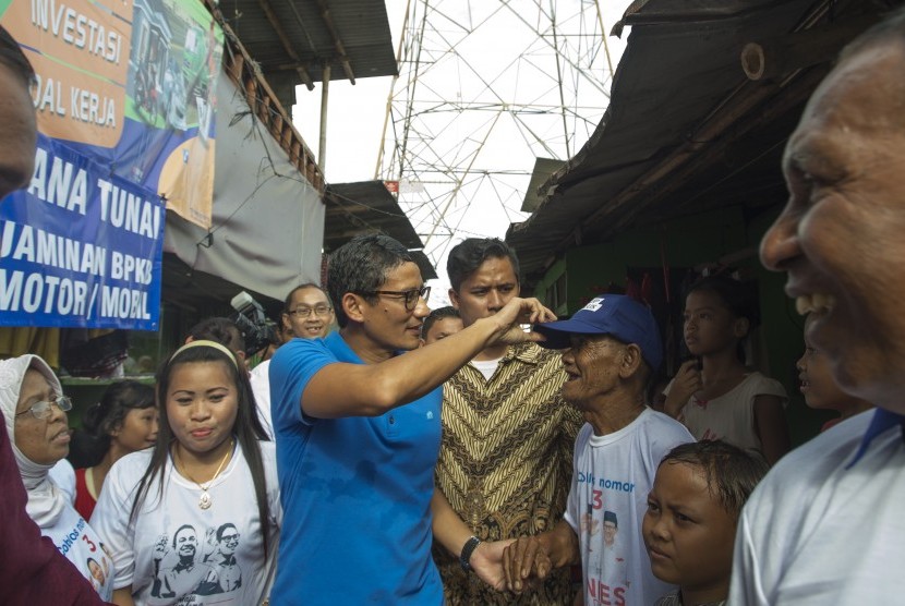 Cawagub DKI Jakarta nomor urut tiga Sandiaga Uno (tengah) memberi topinya kepada warga saat berkampanye di Kampung Kebon Bayam Taman BMW Jakarta, Rabu (25/1). 