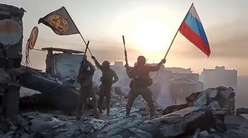 Dalam tangkapan yang diambil dari video yang dirilis oleh Layanan Pers Prigozhin pada hari Sabtu, 20 Mei 2023, anggota perusahaan militer Grup Wagner Yevgeny Prigozhin mengibarkan bendera nasional Rusia dan bendera Wagner di atas sebuah bangunan yang rusak di Bakhmut, Ukraina.