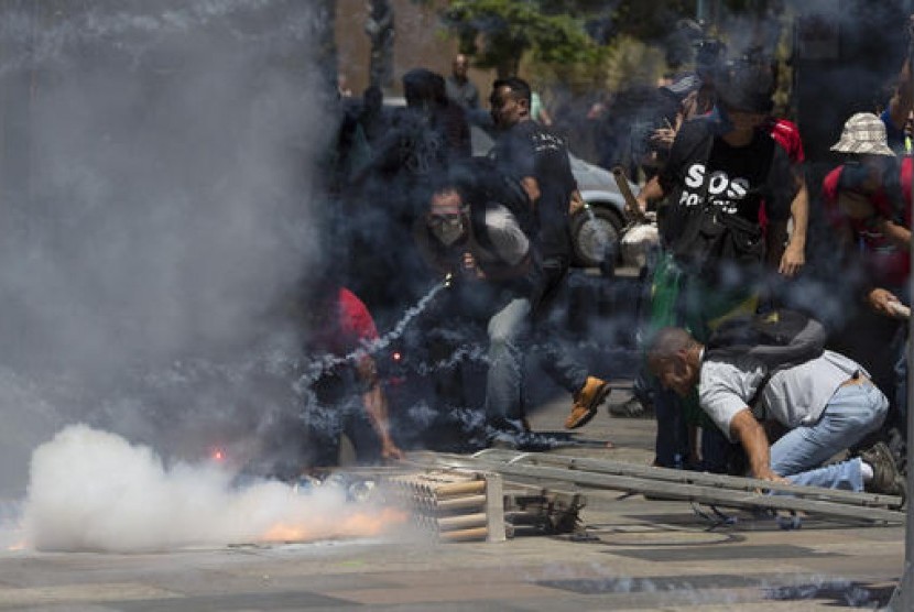 Demonstran antipemotongan upah di Rio de Janeiro, Brasil melempar kembang api ke petugas di depan gedung parlemen, Selasa (6/12). 