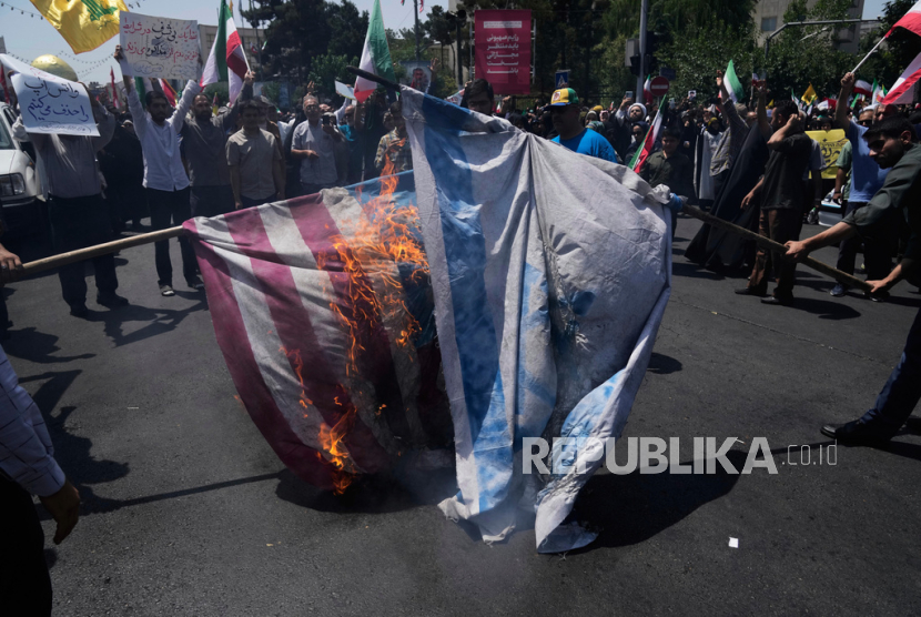 Demonstran membakar bendera Israel dan Amerika Serikat saat menggelar aksi unjuk rasa di Teheran, Iran, Jumat (20/6/2025).
