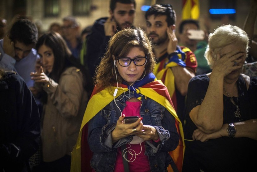 Demonstran mendengarkan pidato Presiden Katalan Carles Puigdemont melalui ponsel di luar Palau Generalitat di Barcelona, Spanyol, Sabtu, 21 Oktober 2017.